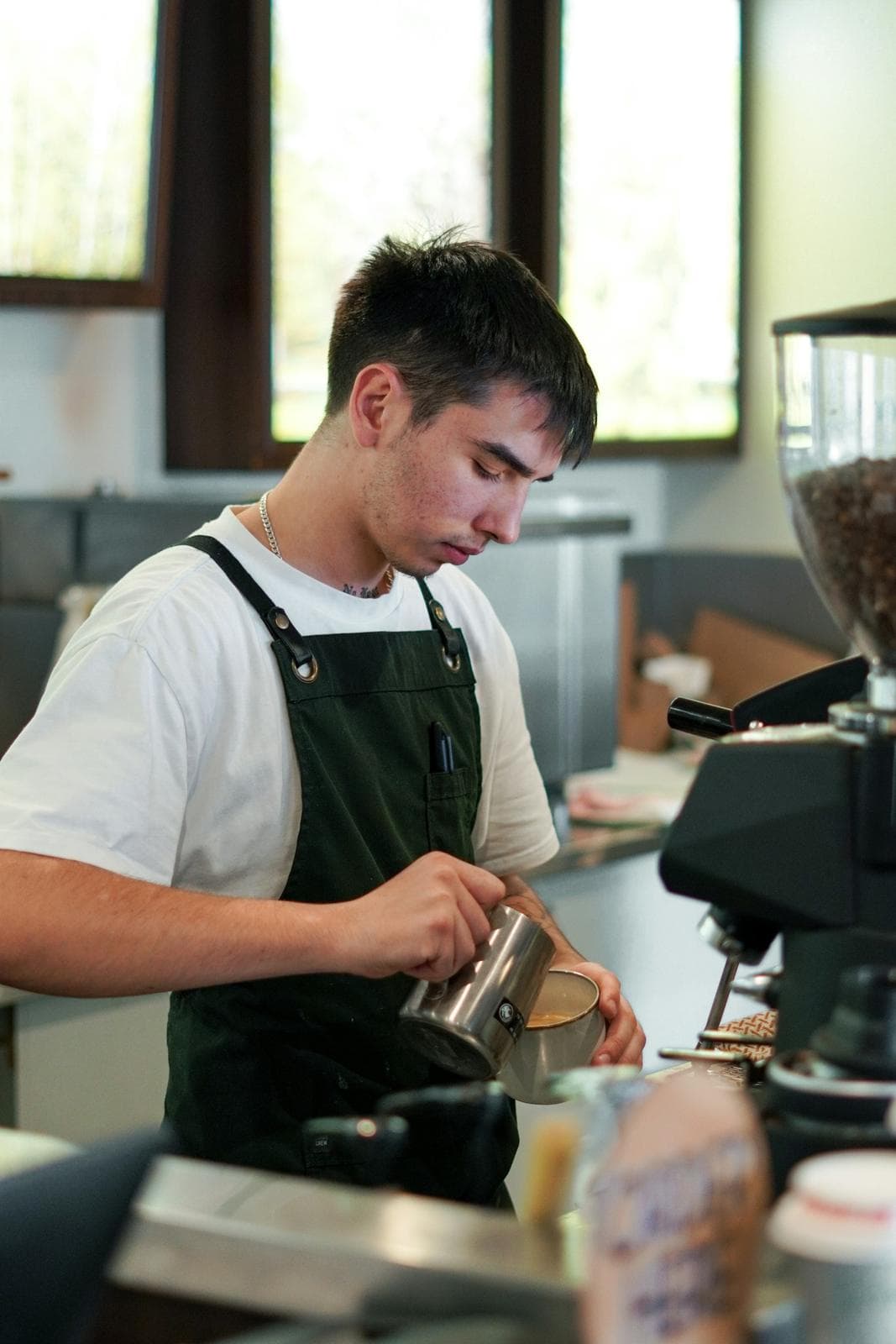 Barista pouring milk behind an espresso machine