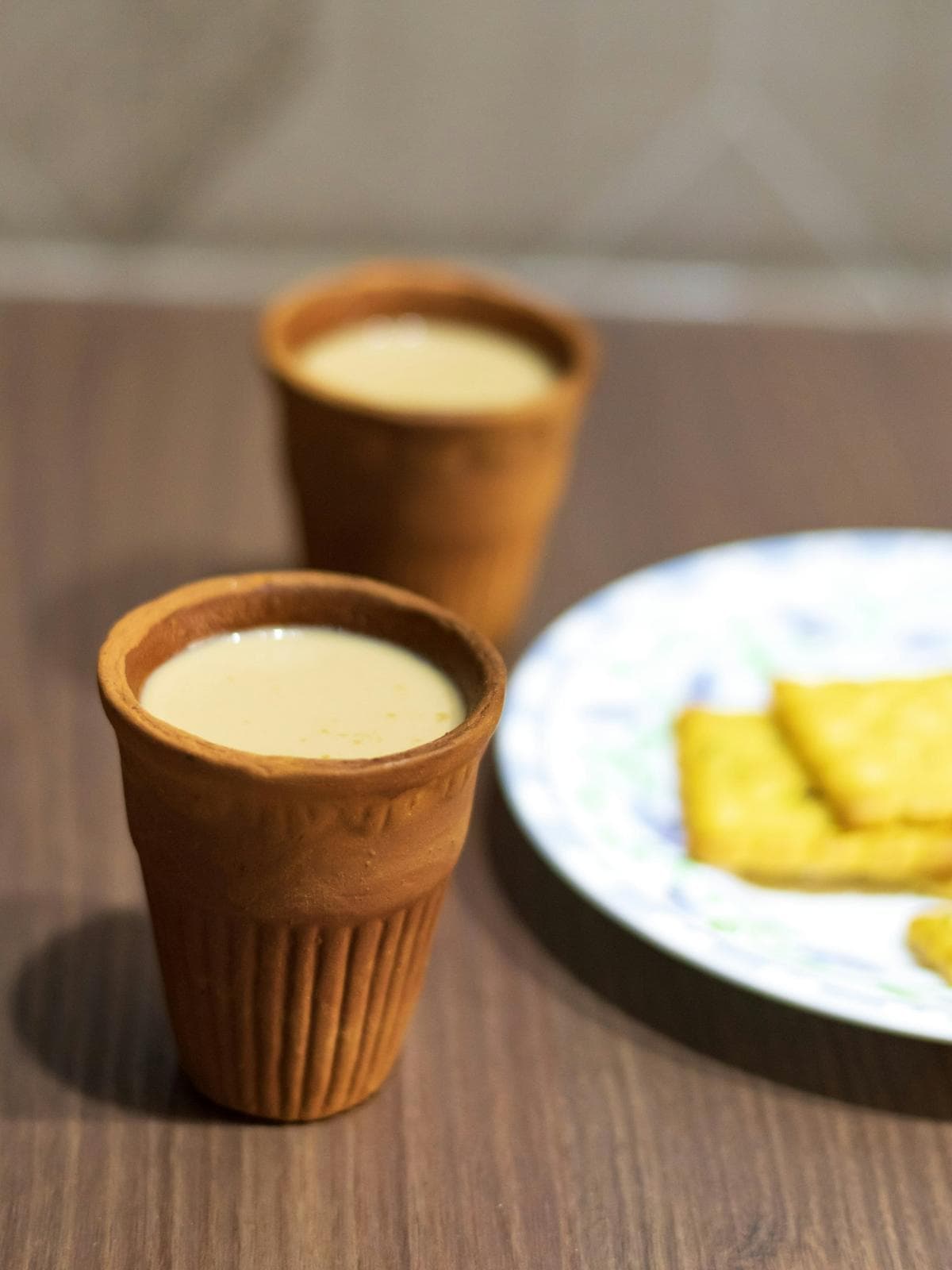 Two clay cups of chai beside a plate of snacks
