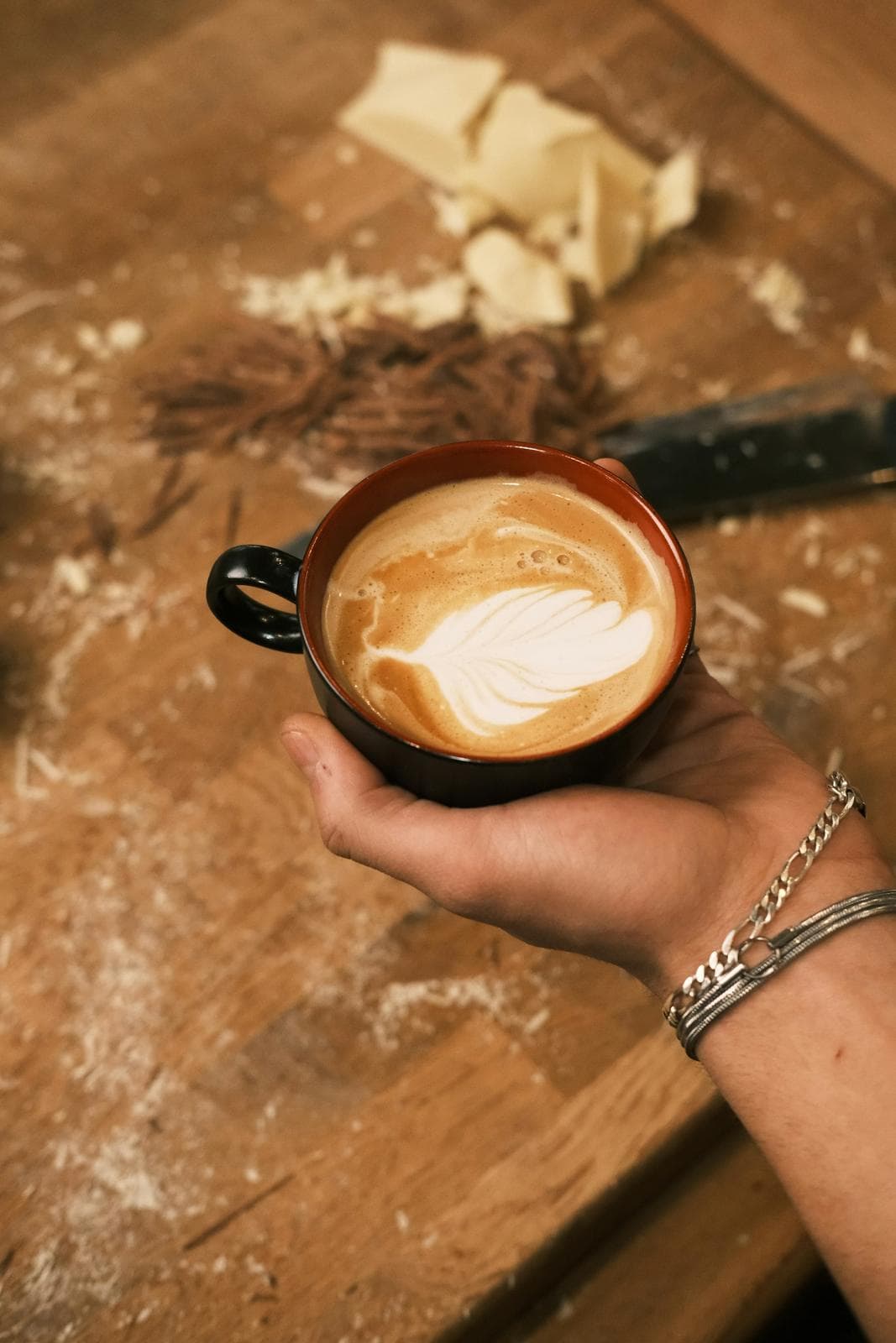 Hands holding a latte with a rosetta on a rustic wooden table