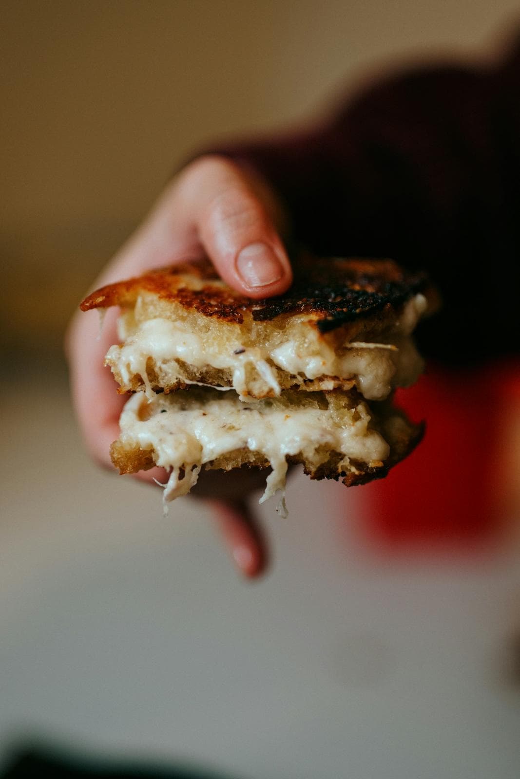 Hand holding a toasted cheese sandwich, cheese oozing at the edges