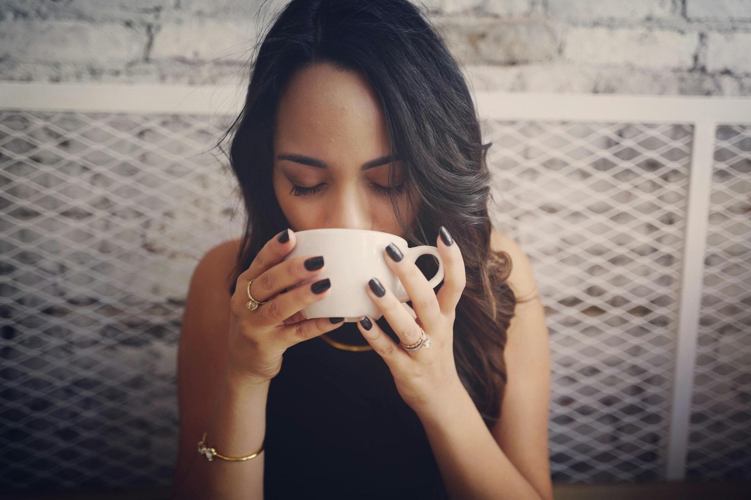 Woman with eyes closed taking the first sip from a white coffee cup held in both hands