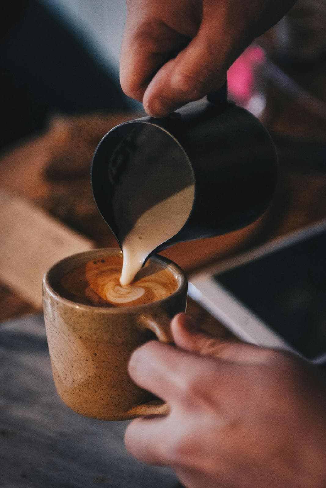 Milk being poured into a cup of coffee held at a café counter