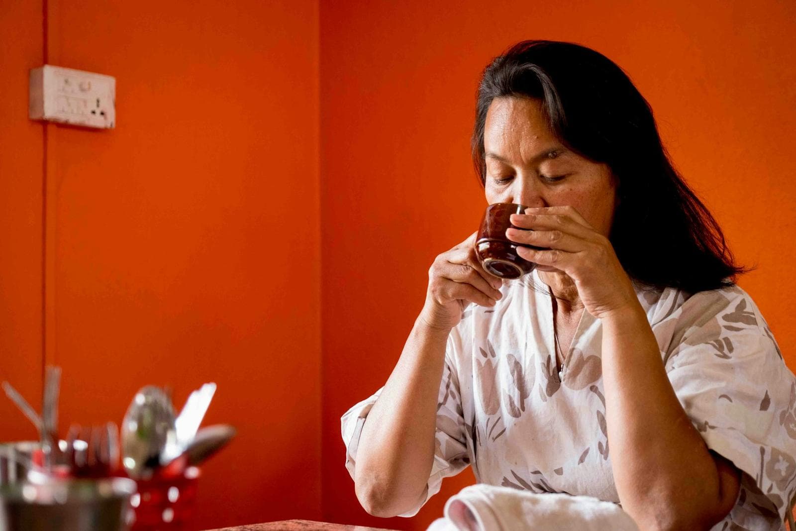 Woman drinking coffee at a table against an orange wall