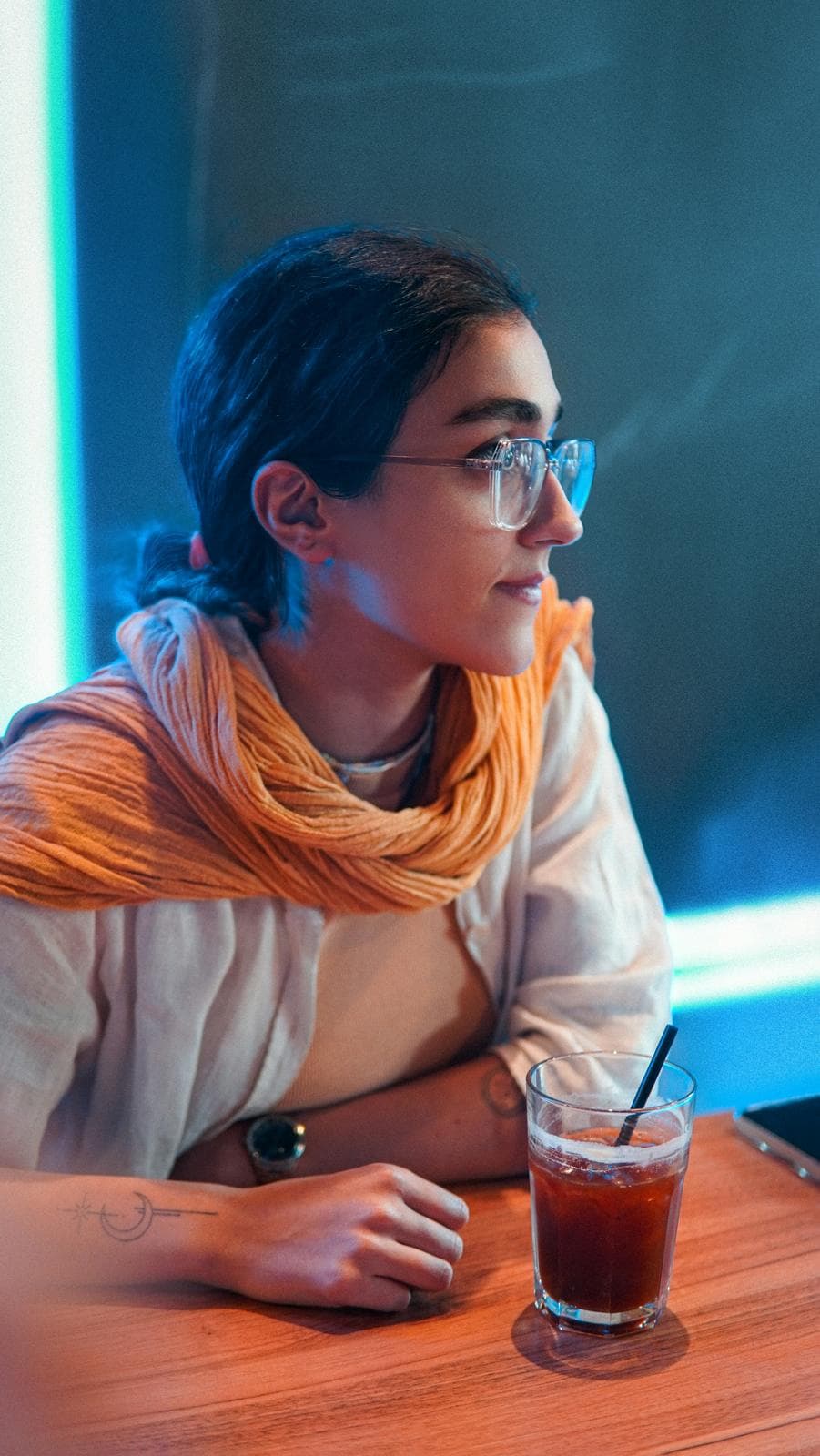 Woman in an orange scarf at a café table with an iced coffee