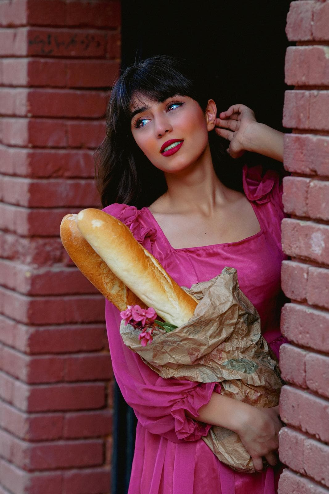 Woman in a pink dress against a brick wall holding a fresh loaf